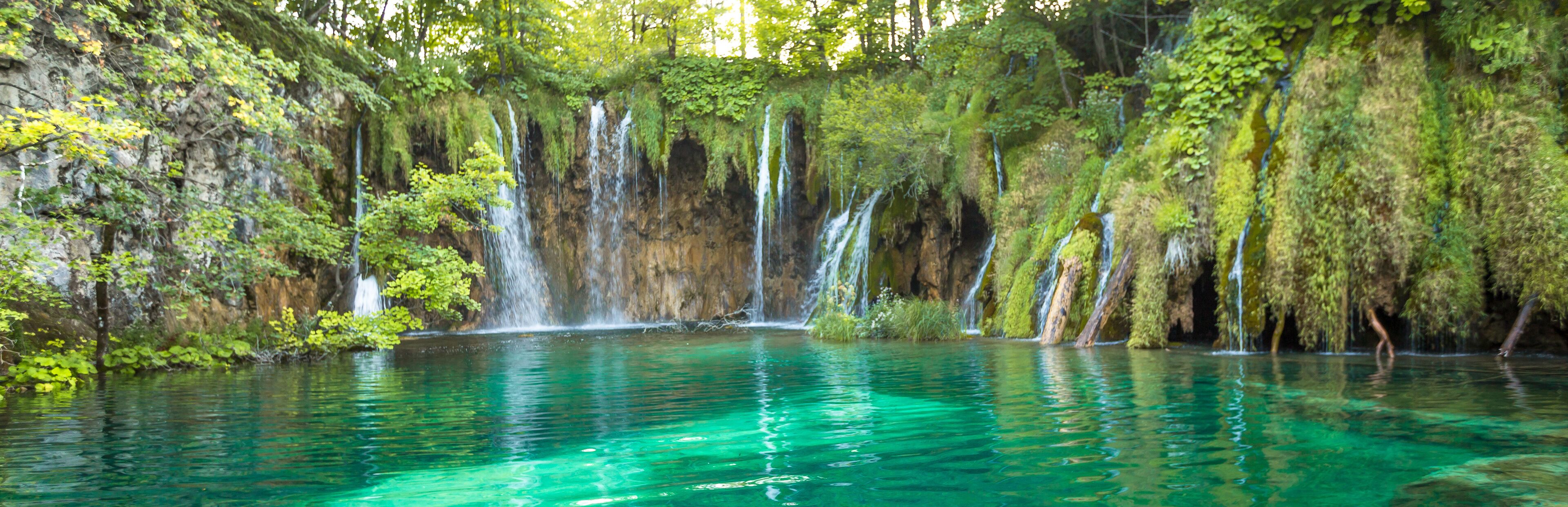 A waterfall cascading into a clear turquoise pool surrounded by lush greenery.