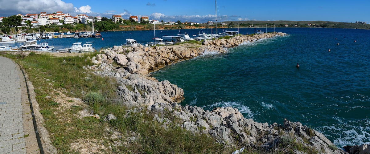 A coastal marina with boats, rocky shoreline, and houses in the background.