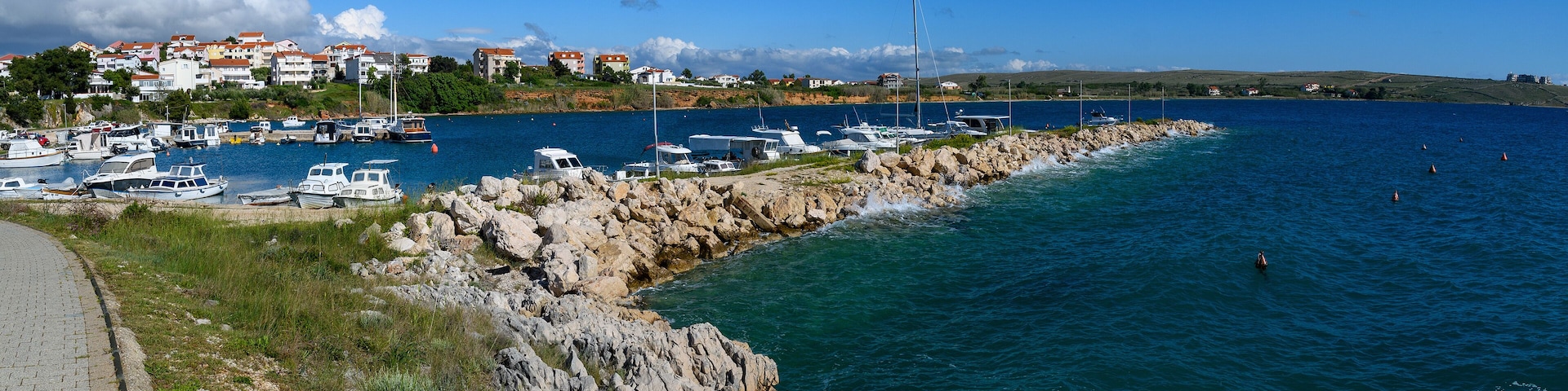 A coastal marina with boats, rocky shoreline, and houses in the background.
