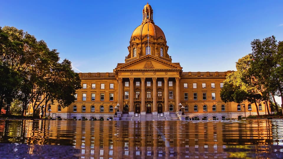 A large, classical building with a prominent dome and columns, reflecting in a body of water.