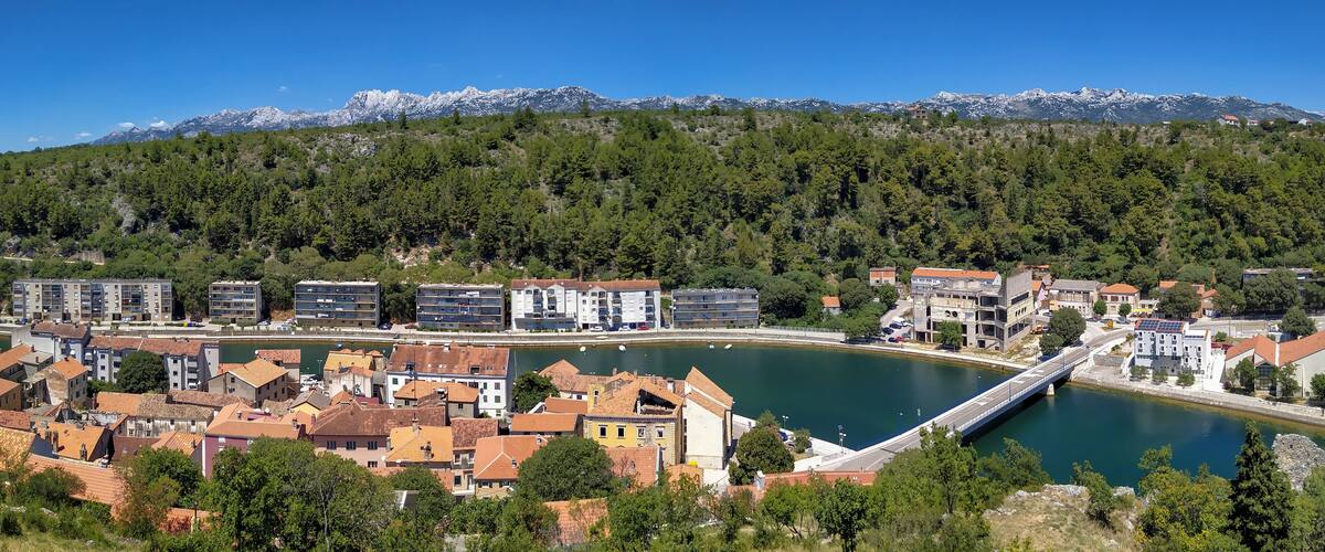 A coastal town with a bridge over a river, surrounded by mountains and dense forests.