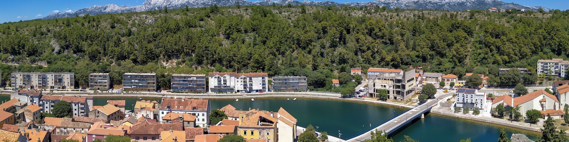 A coastal town with a bridge over a river, surrounded by mountains and dense forests.