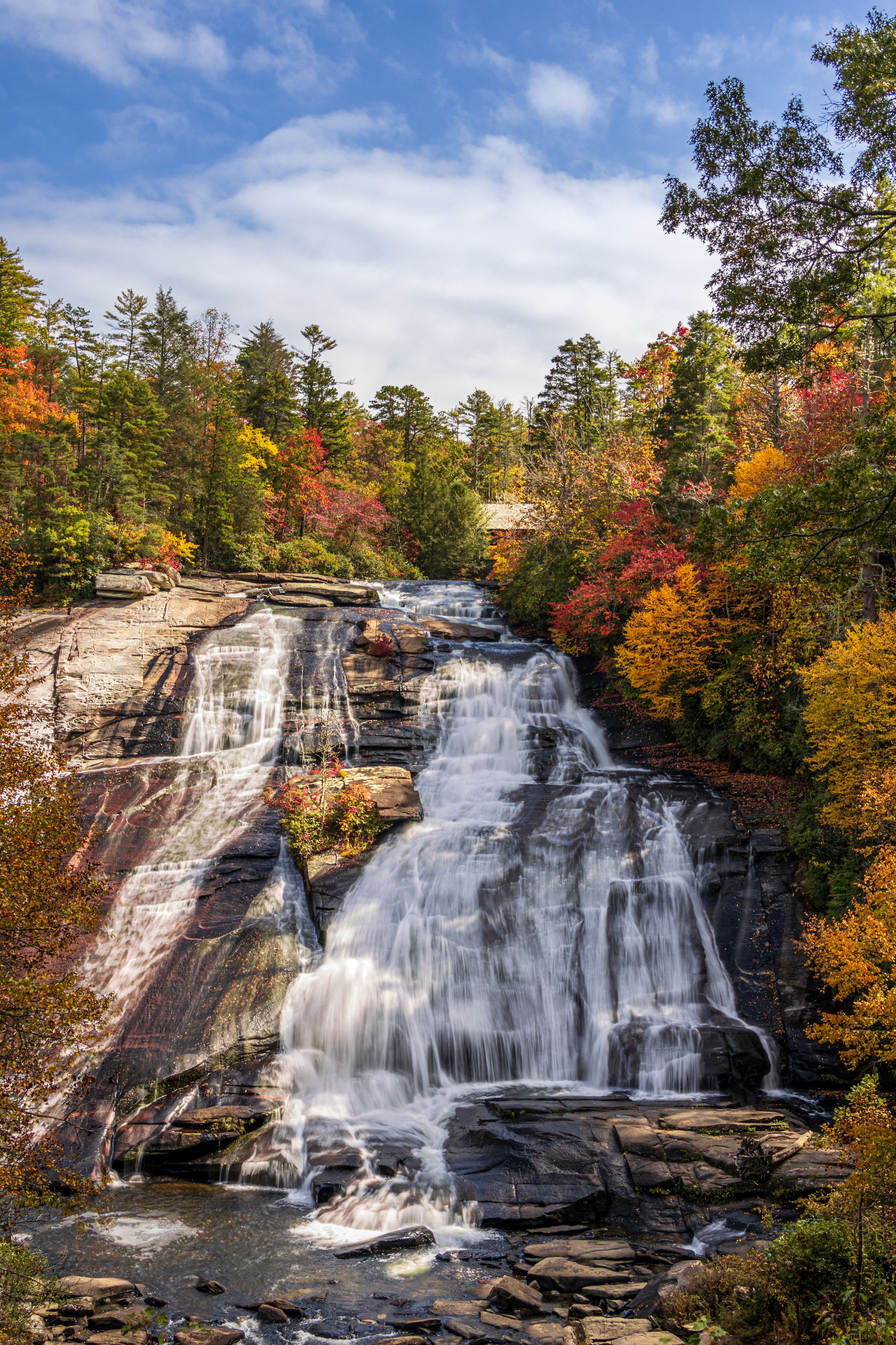 A multi-tiered waterfall cascading over rocky terrain, surrounded by autumn-colored foliage.