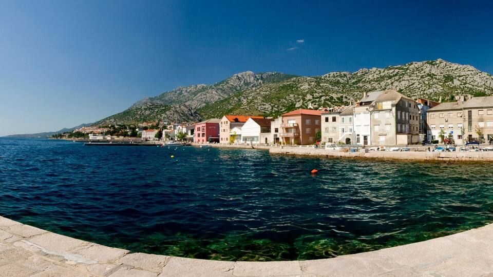 A coastal town with a clear blue sea, stone buildings, and a mountain in the background.