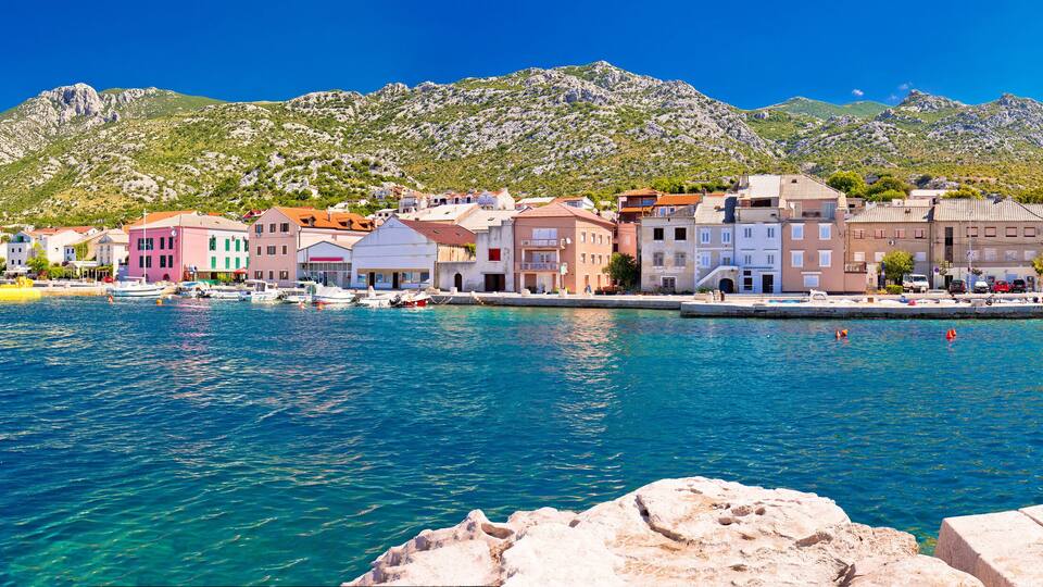 A coastal town with colorful buildings, a clear blue sea, and mountains in the background.