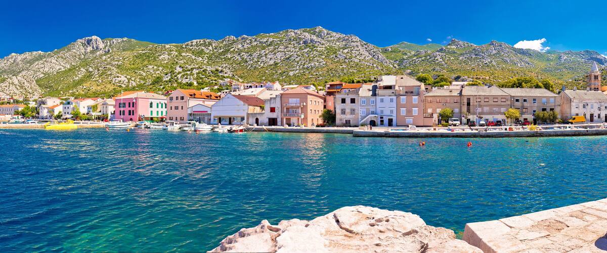A coastal town with colorful buildings, a clear blue sea, and mountains in the background.