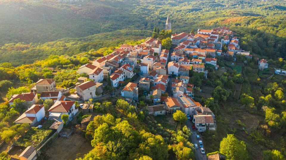 An aerial view of a village with red-roofed houses nestled in a valley surrounded by greenery.