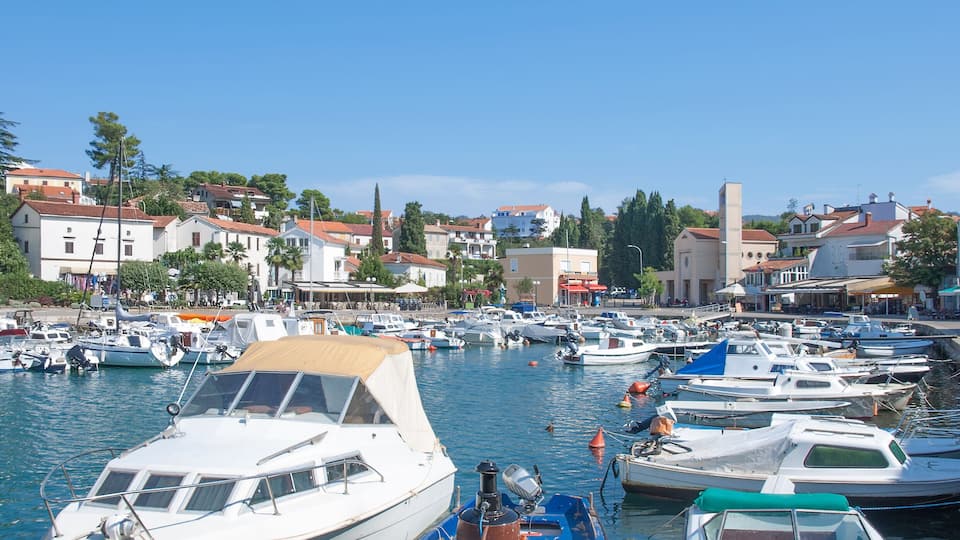 A marina with various boats docked, a clear blue sky, and buildings in the background.
