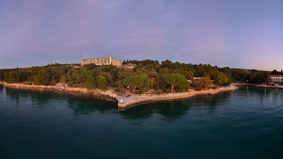 A coastal island with a large building, dense trees, and calm water.