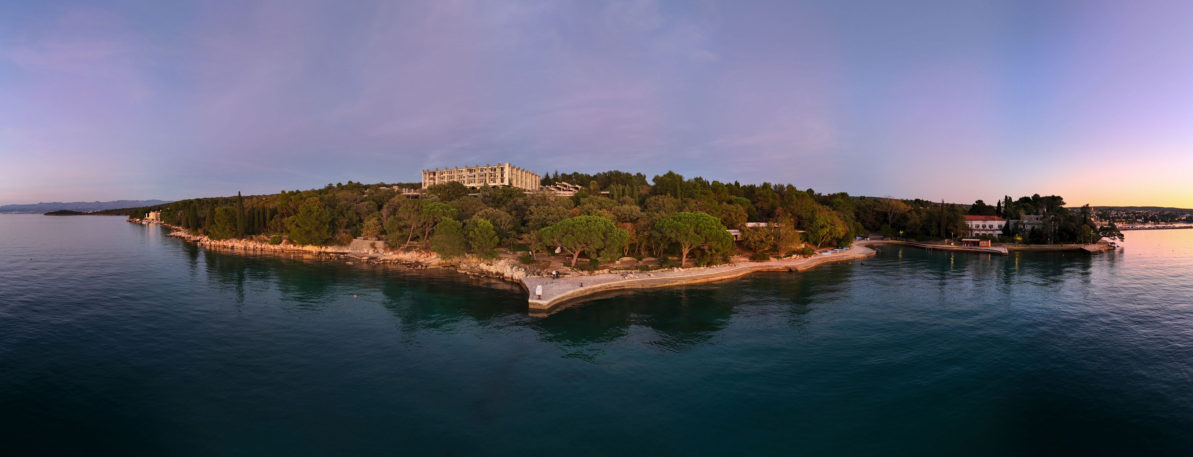 A coastal island with a large building, dense trees, and calm water.