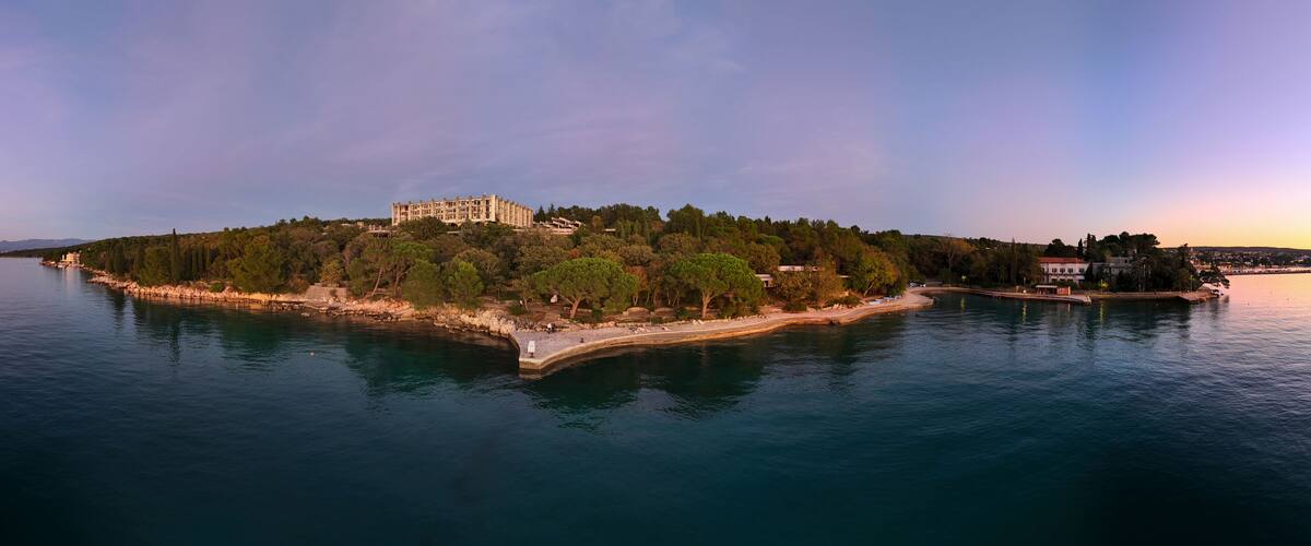 A coastal island with a large building, dense trees, and calm water.