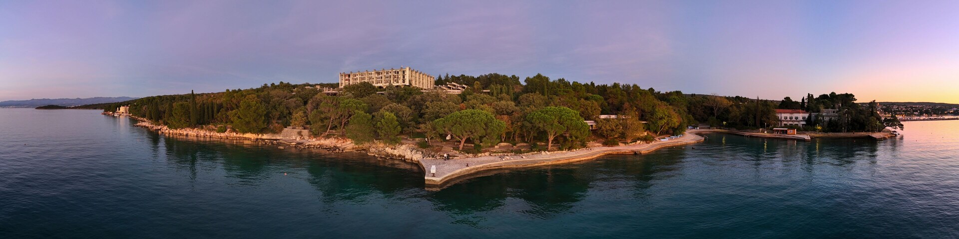 A coastal island with a large building, dense trees, and calm water.