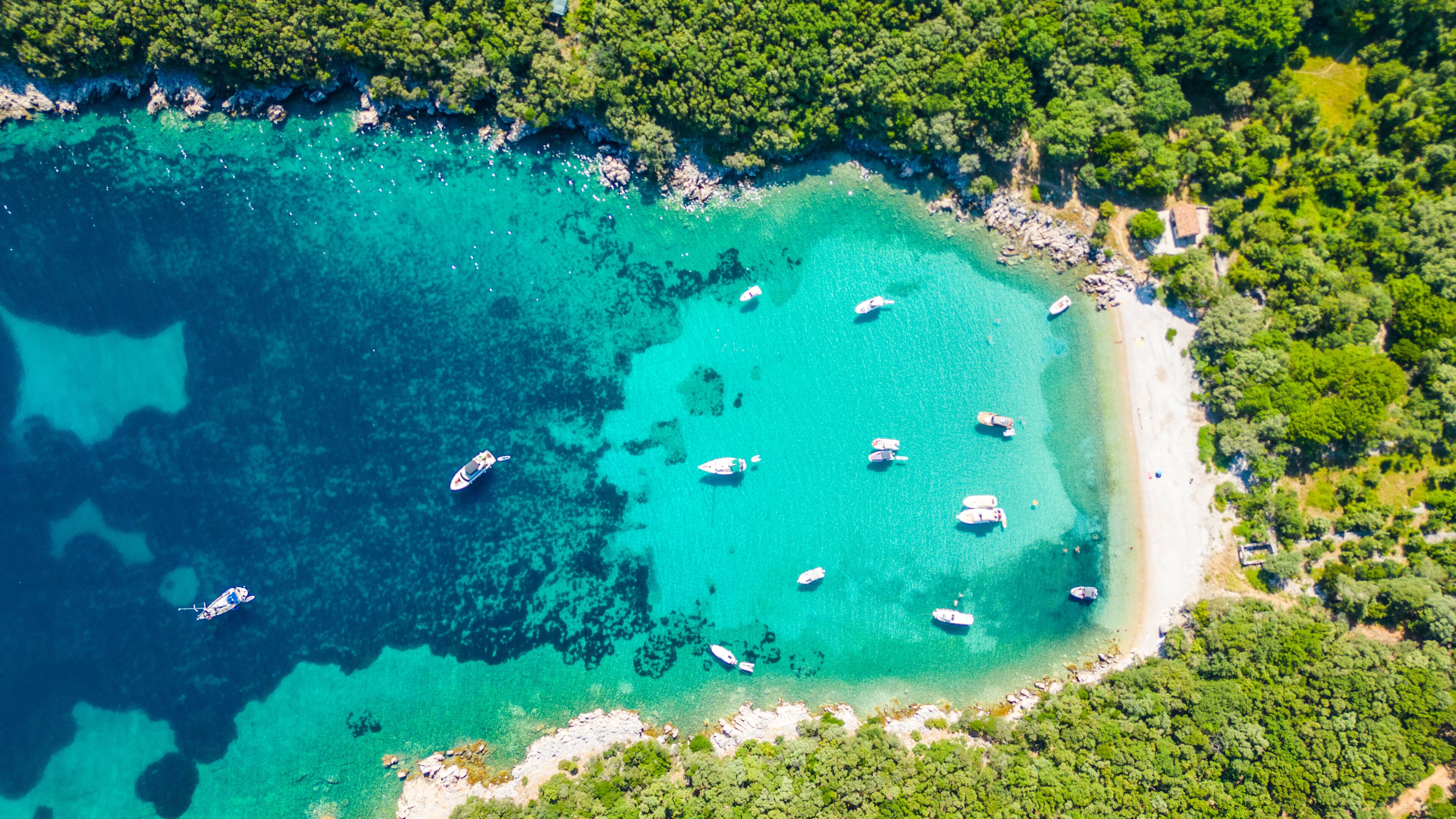 A turquoise coastal area with boats anchored near the shore, surrounded by dense green vegetation.