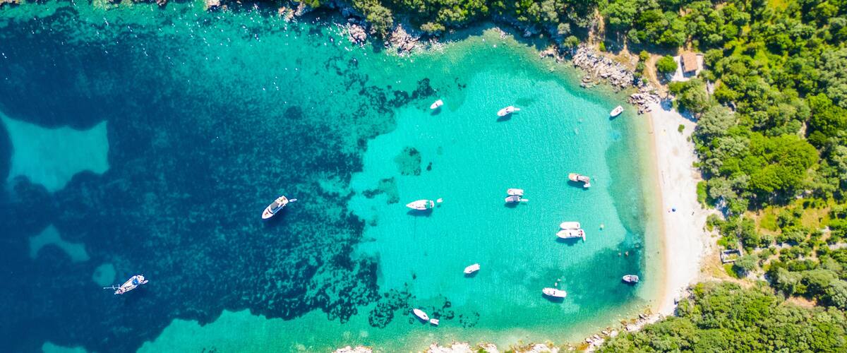 A turquoise coastal area with boats anchored near the shore, surrounded by dense green vegetation.