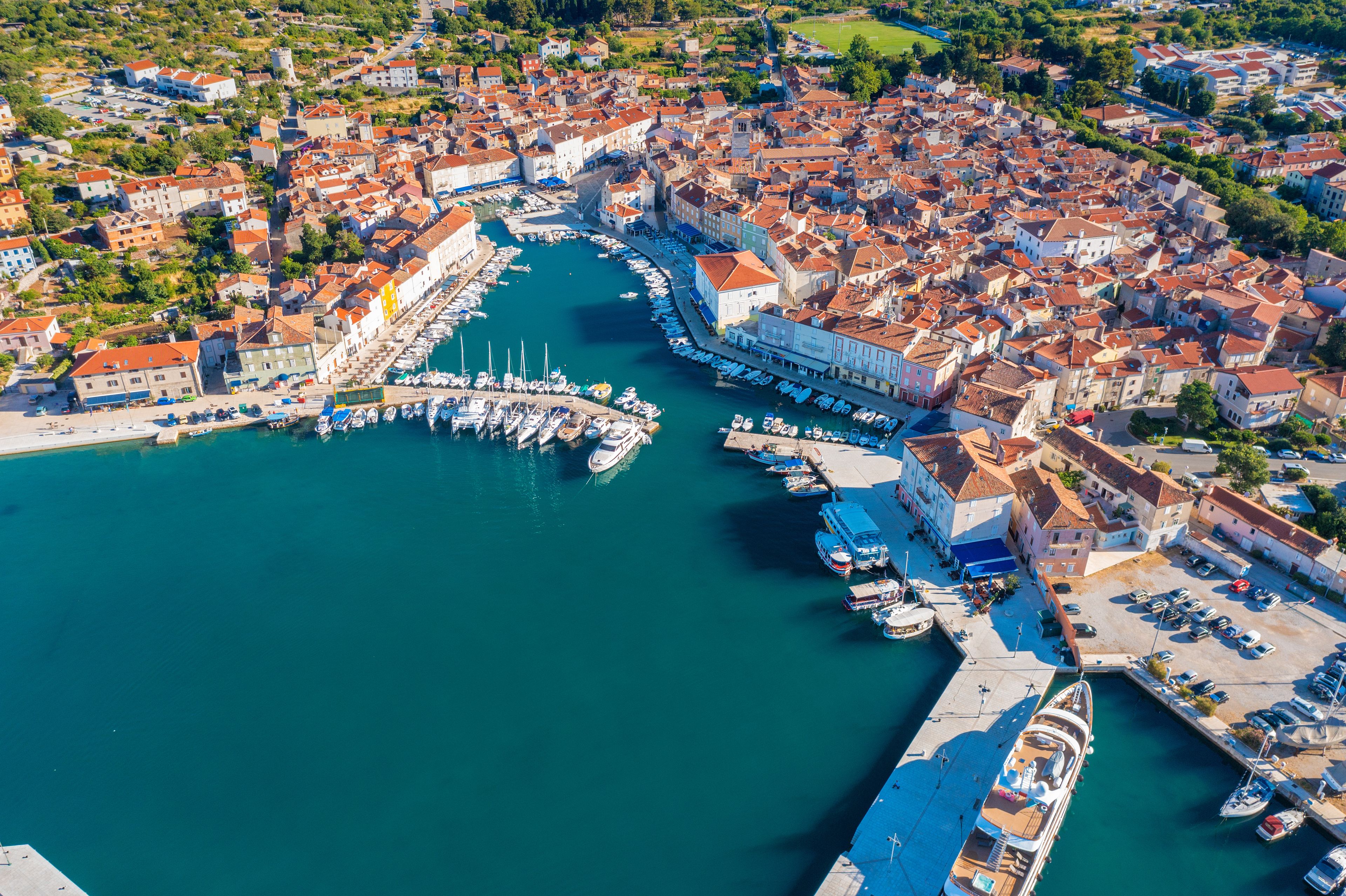 Un pueblo costero con un puerto deportivo, casas escalonadas y un puerto azul cristalino.