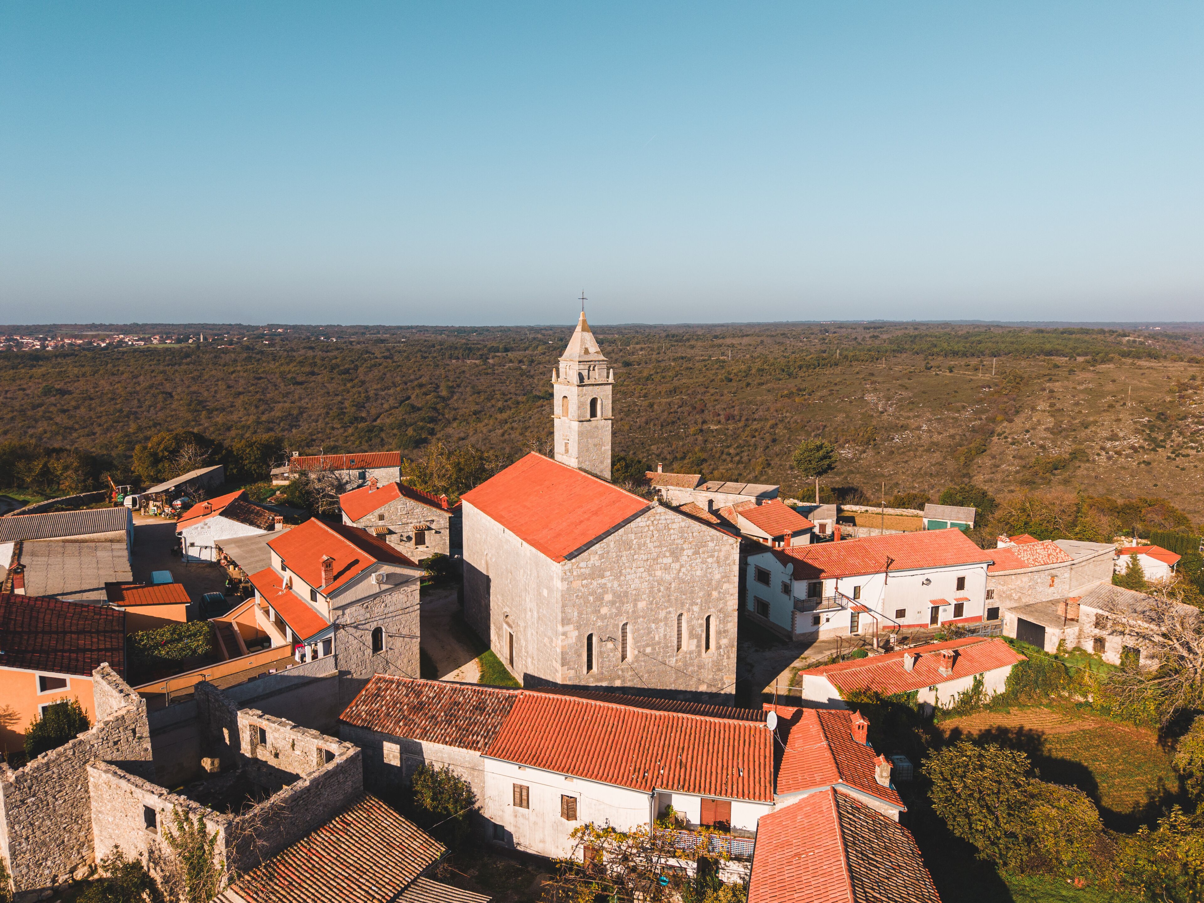 Aerial view of sun-kissed red rooftops and the towering church spire amidst the stone buildings, contrasting against the lush green landscape, Marcana, Istria County, Croatia.