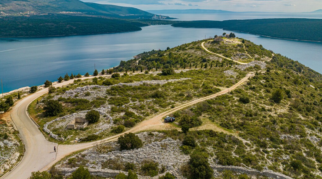 Aerial view of a winding road leading to a historic site atop a rugged peninsula, embraced by the tranquil Adriatic Sea, Rakalj, Sv. Agnija, Istria County, Croatia.