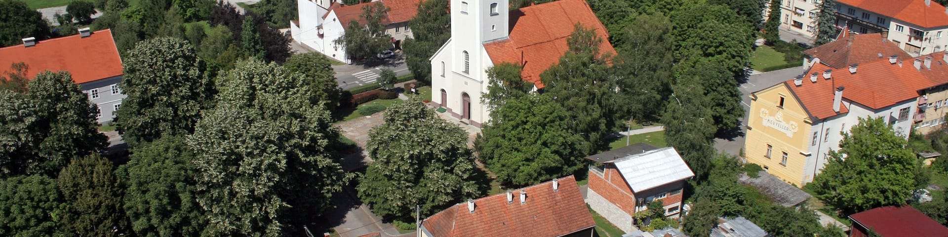 A town with red-roofed houses, a church with a tower, and surrounding green fields.