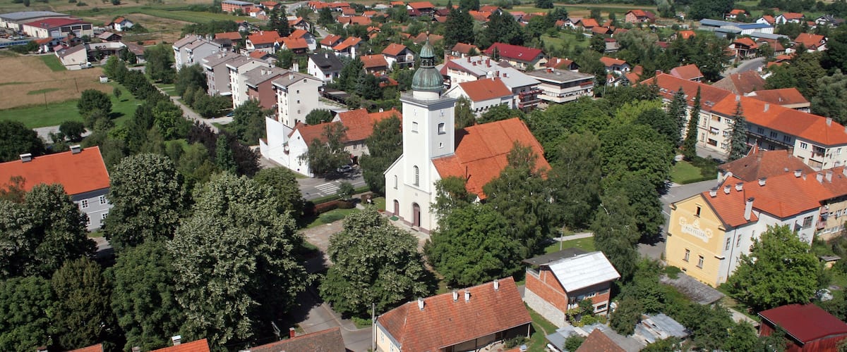 A town with red-roofed houses, a church with a tower, and surrounding green fields.