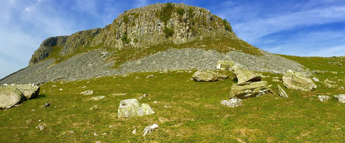 A grassy hill with large boulders and a rocky cliff.