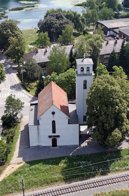 A white church with a bell tower, surrounded by trees and a lake.