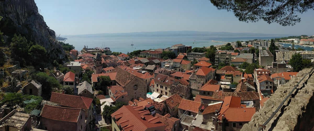 A coastal town with red-tiled roofs, a rocky cliff, and a clear view of the sea.
