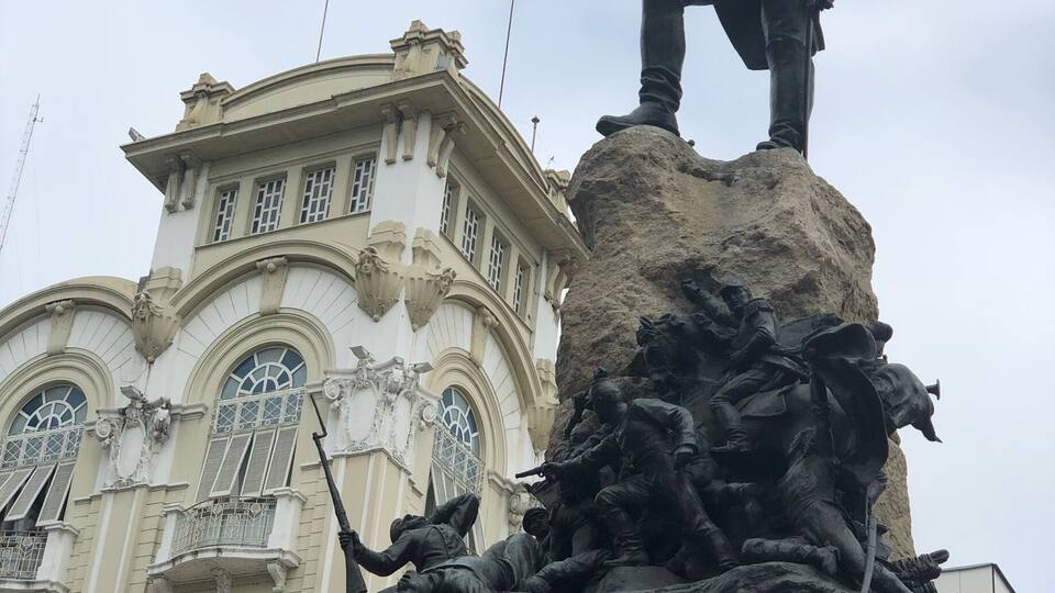 A statue of a soldier on a pedestal with a building in the background.