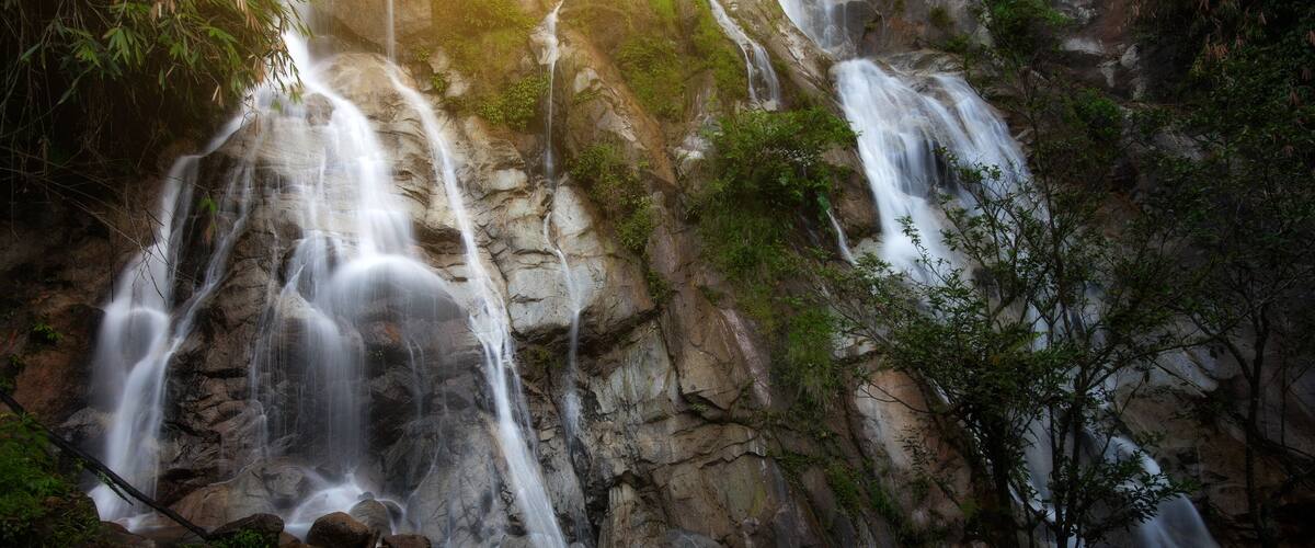 A multi-tiered waterfall cascading over rocky terrain with lush greenery.