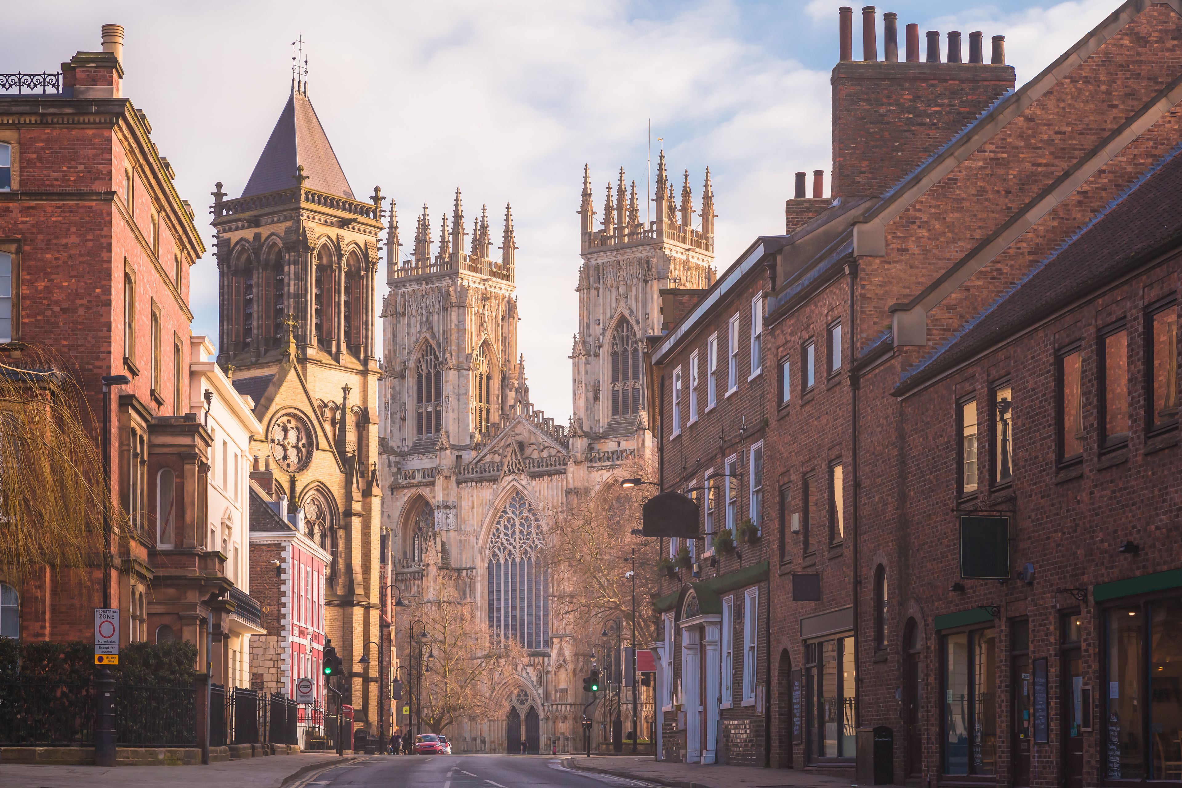 A historic street with Gothic architecture, including a prominent church with a tall spire and intricate stonework.