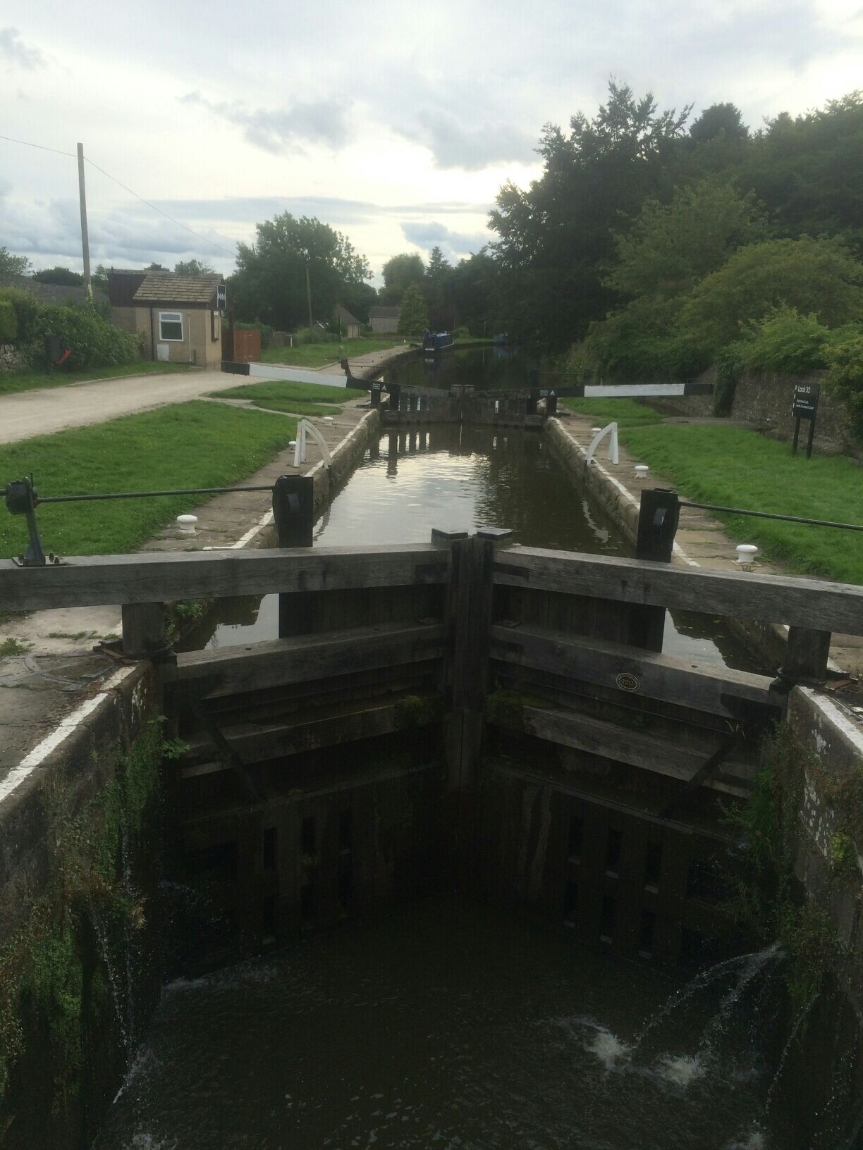 A narrow canal with a wooden gate, surrounded by greenery and a small building in the background.