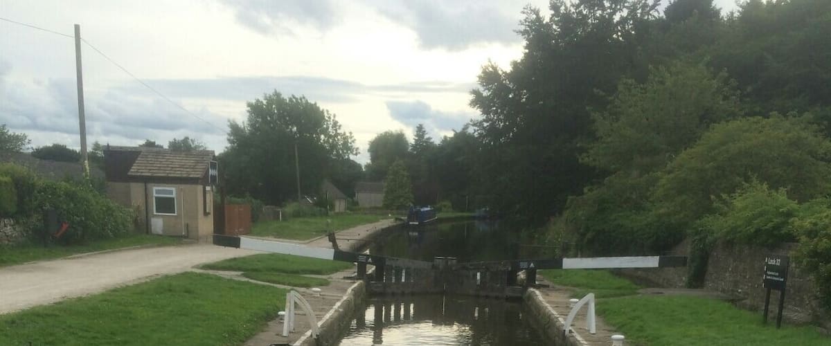 A narrow canal with a wooden gate, surrounded by greenery and a small building in the background.