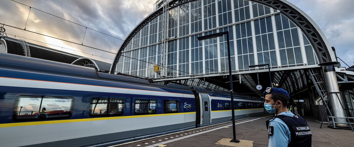 A train at a station with a large glass building in the background.