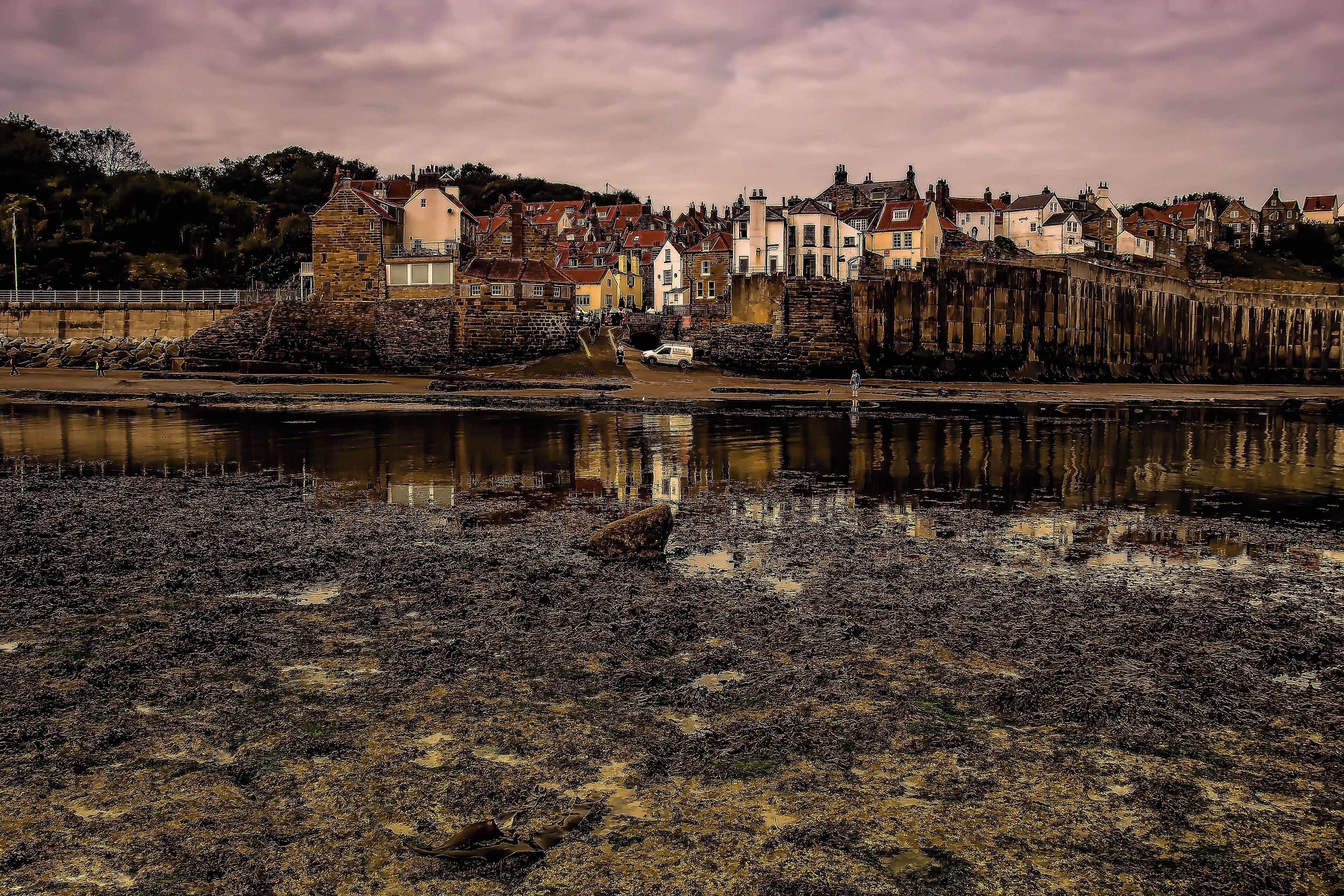 A coastal town with historic buildings, a stone wall, and a body of water reflecting the structures.