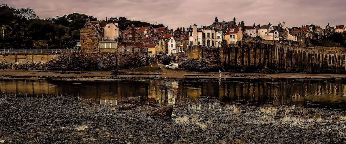 A coastal town with historic buildings, a stone wall, and a body of water reflecting the structures.