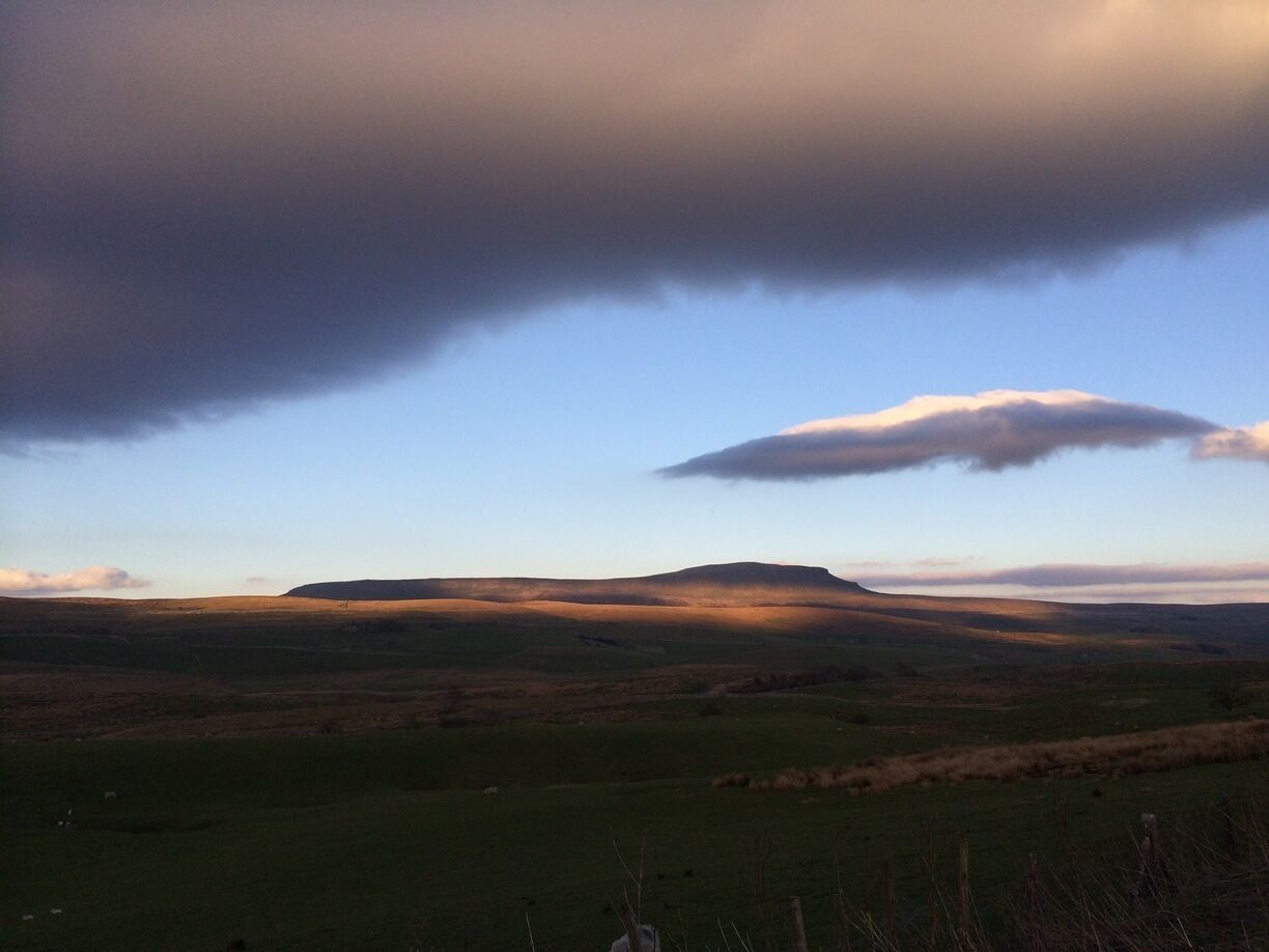 A rolling landscape with a prominent hill in the center, under a partly cloudy sky.