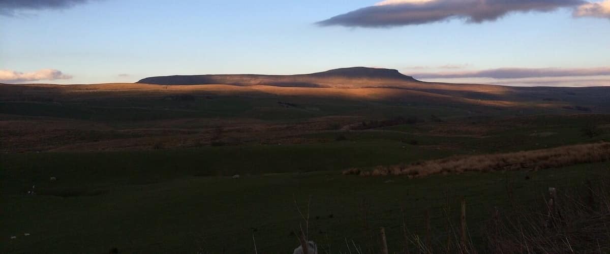 A rolling landscape with a prominent hill in the center, under a partly cloudy sky.