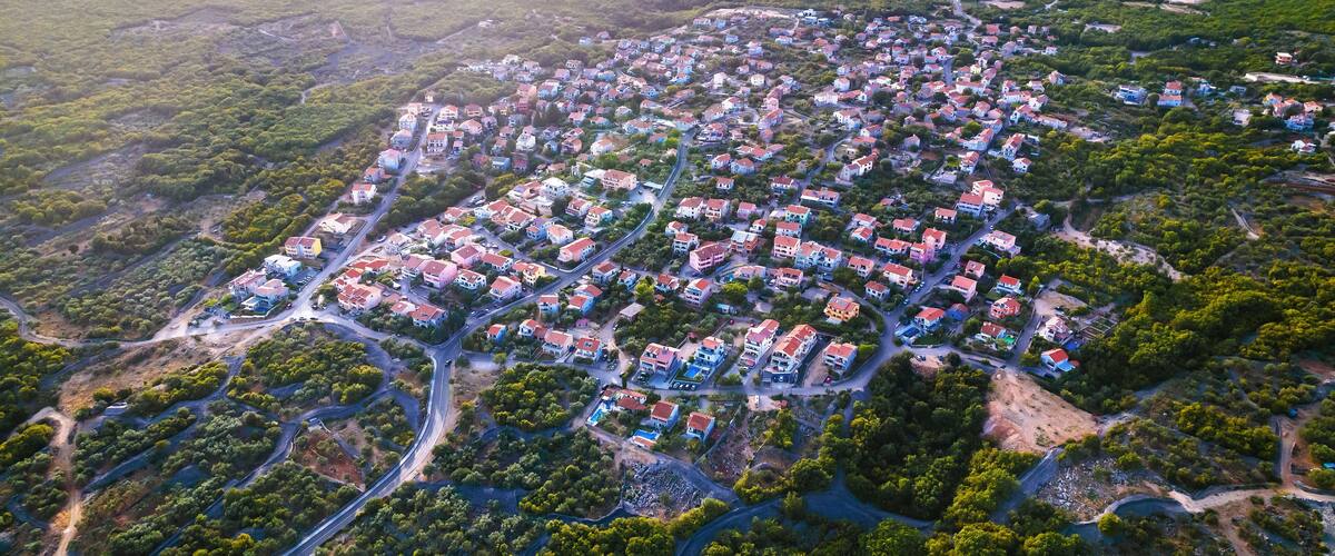 An aerial view of a residential area with houses, roads, and surrounding greenery.