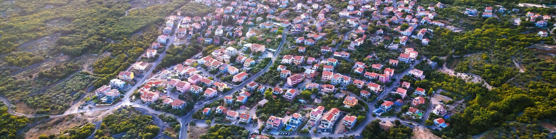 An aerial view of a residential area with houses, roads, and surrounding greenery.