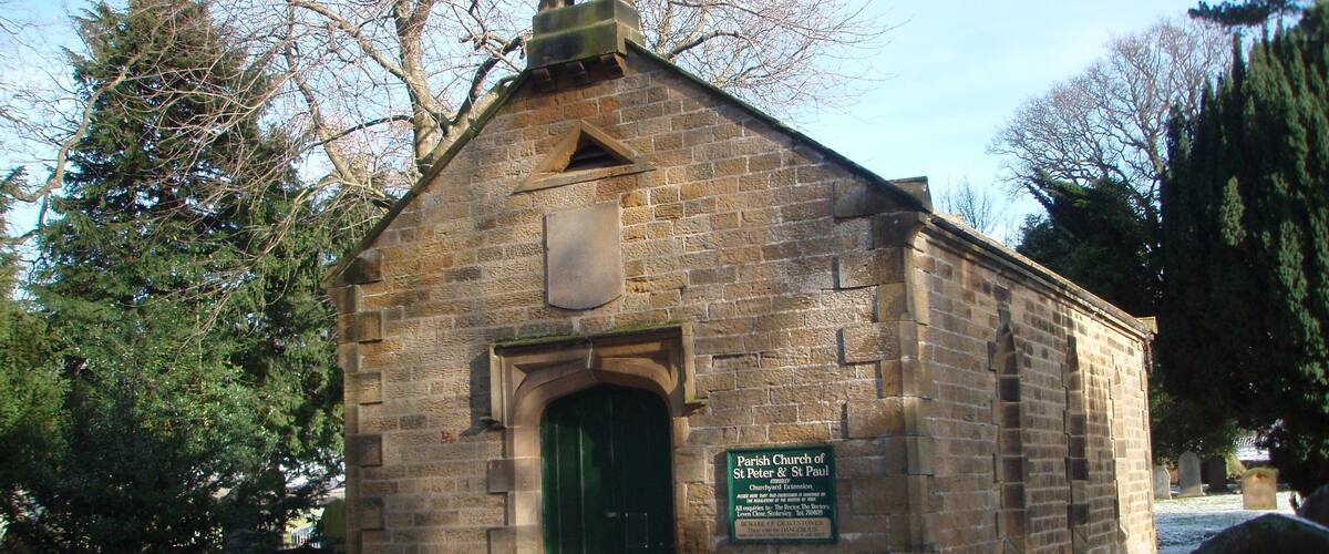 A small stone church with a green door and a sign indicating it is the Parish Church of St Peter & St Paul.