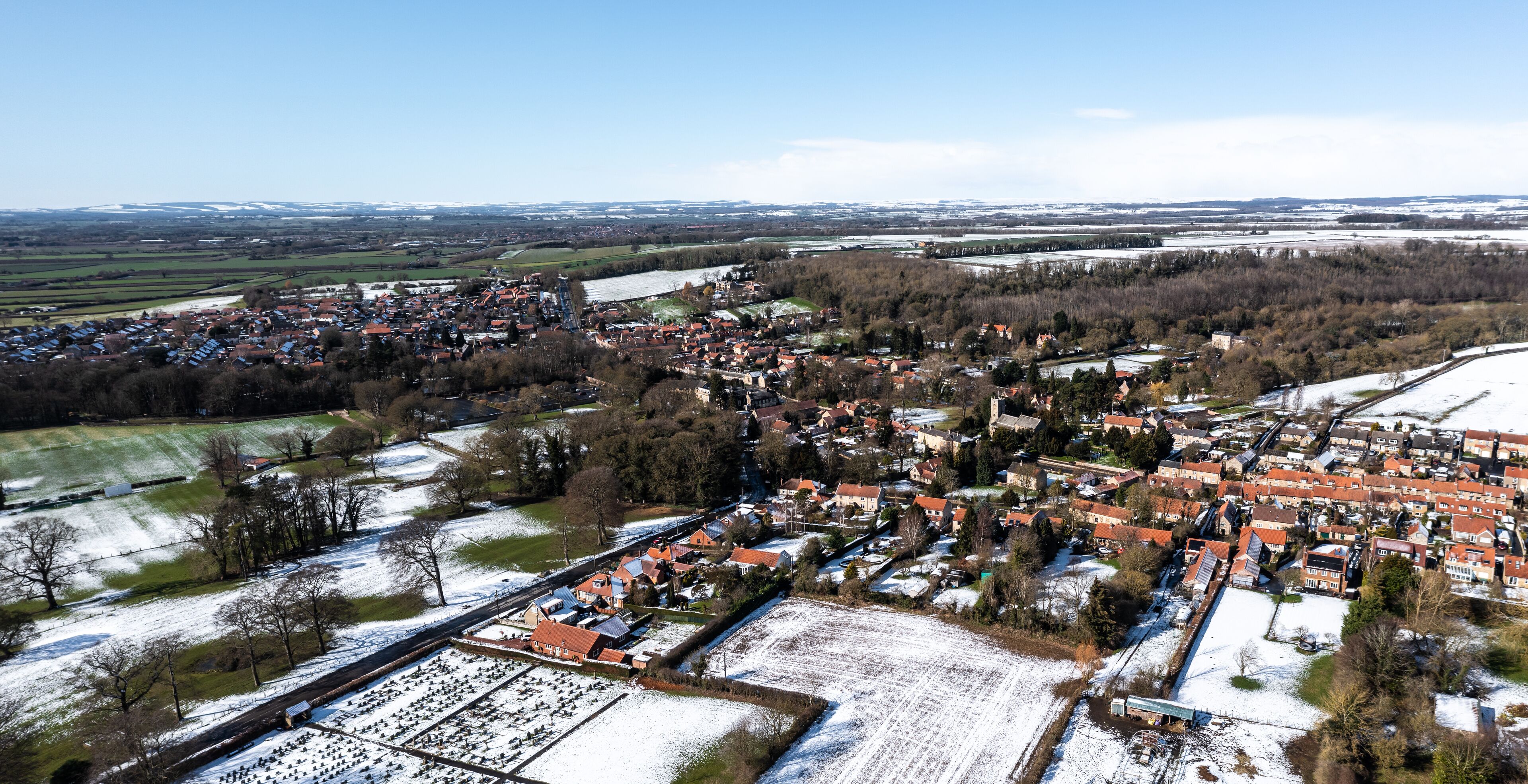 A snow-covered town with red-roofed houses, a river, and surrounding fields.