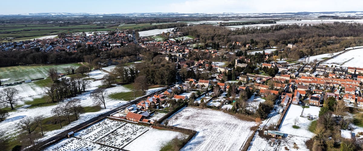 A snow-covered town with red-roofed houses, a river, and surrounding fields.