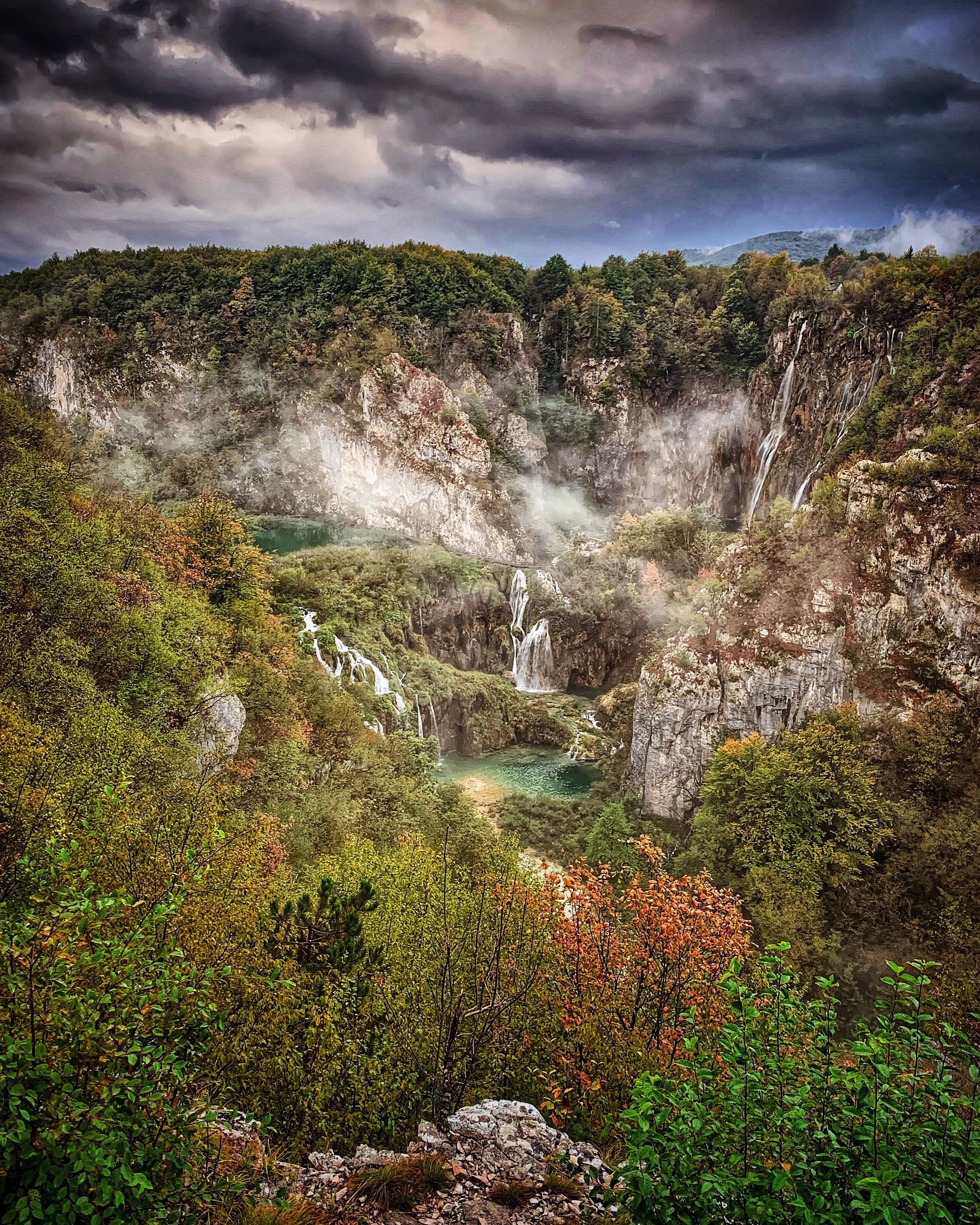 A mountainous landscape with multiple waterfalls, dense forest, and a river.