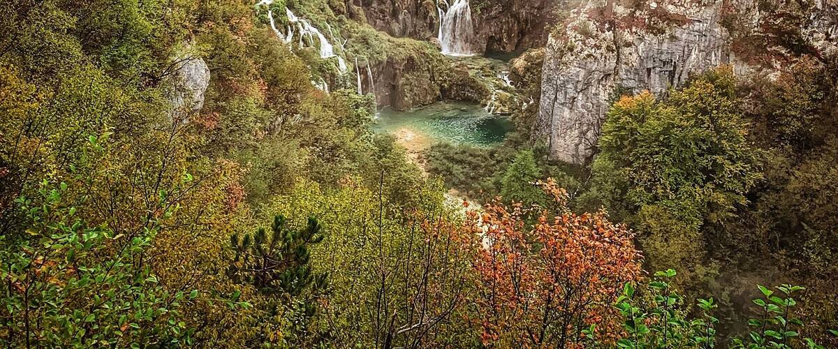 A mountainous landscape with multiple waterfalls, dense forest, and a river.