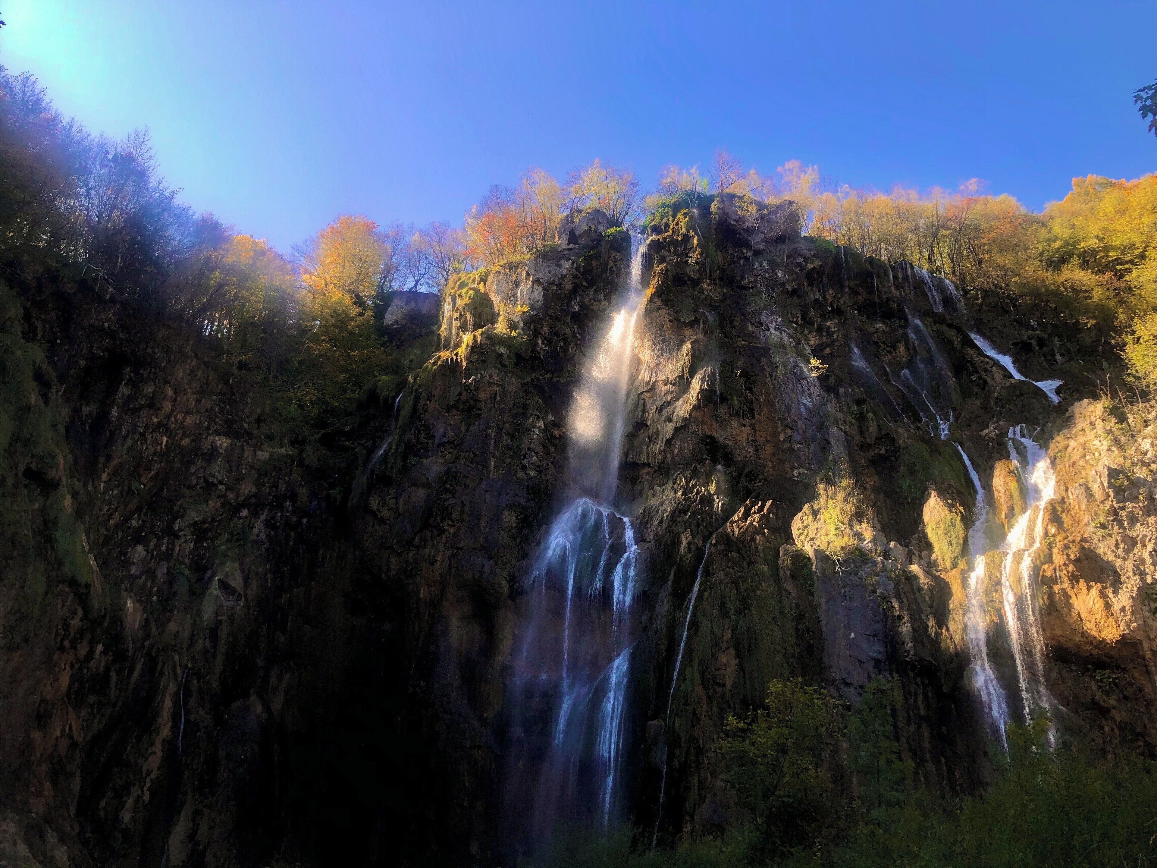 A waterfall cascading down a rocky cliff surrounded by autumn-colored trees.