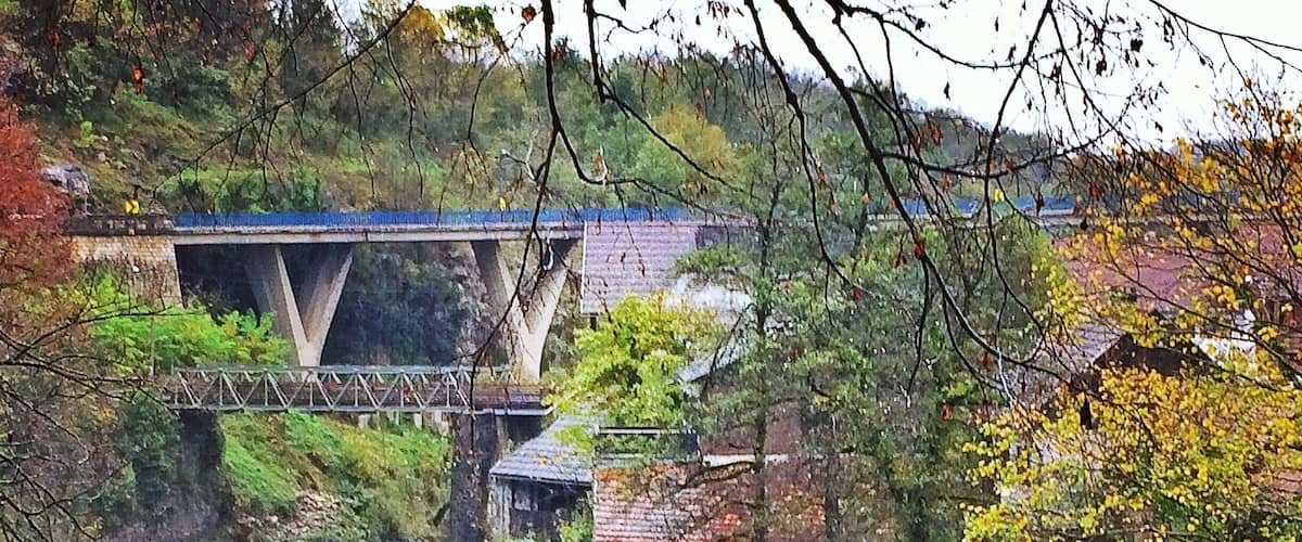 A river flowing under a bridge surrounded by trees and greenery.