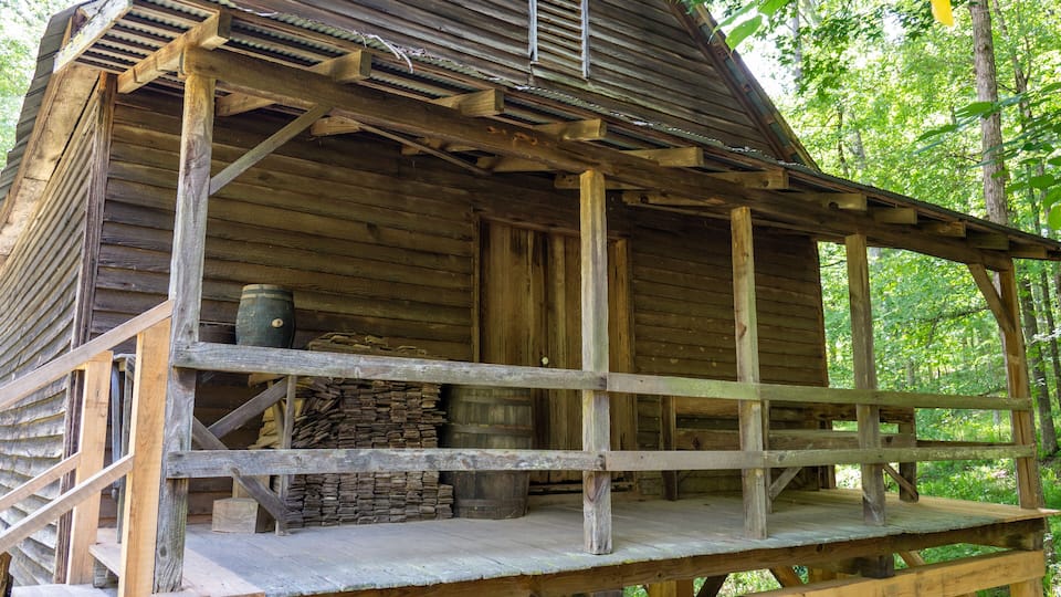A rustic wooden cabin with a porch, surrounded by a forest.
