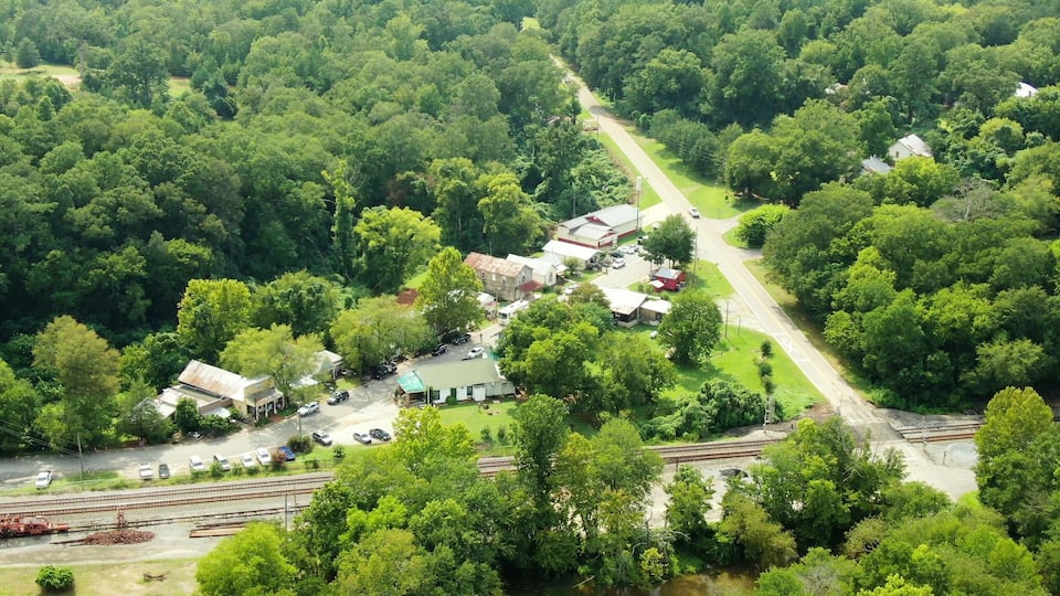 An aerial view of a small town with a railway track, surrounded by dense greenery and a few buildings.