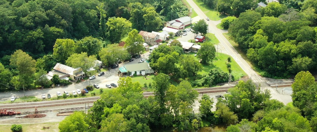 An aerial view of a small town with a railway track, surrounded by dense greenery and a few buildings.