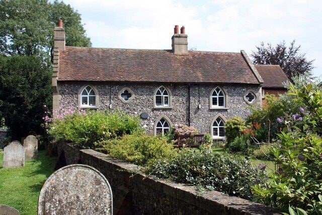 A stone house with a tiled roof, surrounded by a garden and a stone wall.