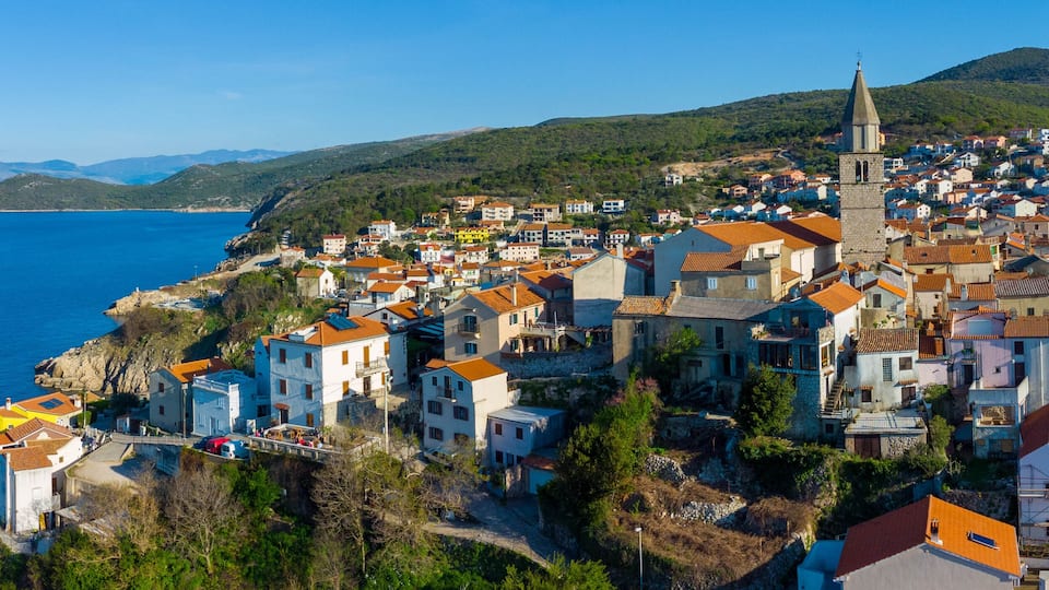 A coastal town with a prominent church tower, colorful buildings, and a clear view of the sea.